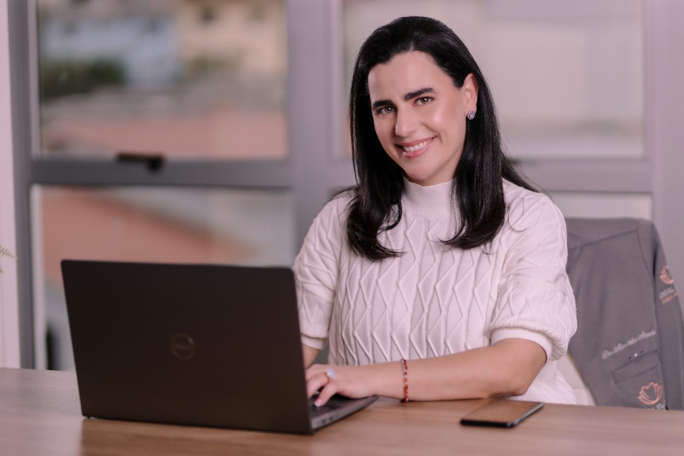 Dentista da Oral Flora sorrindo à mesa de trabalho, com notebook